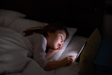 six years old girl lying on white bed at night touching digital screen mobile phone