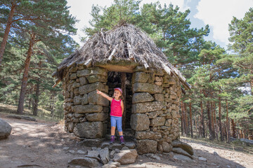little girl pointing with finger n the door frame of ancient hut in forest of Madrid mountain