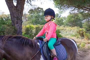 side view of little girl riding a horse in a forest