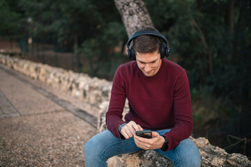Boy listening to music with wireless headphones and using his cell phone sitting down.