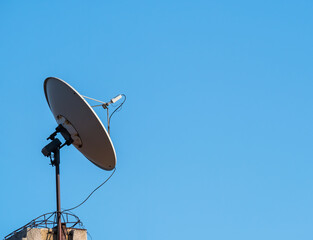 Satellite dish or parabolic antenna on the roof of a building against blue sky.