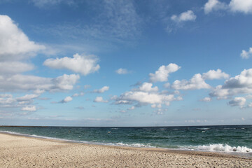 Fototapeta na wymiar Marine autumn landscape. Sandy coast, turquoise sea with small waves and blue cloudy sky.