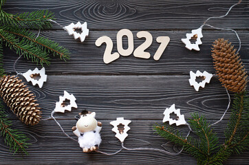 Obraz na płótnie Canvas Christmas tree branches with a garland and the number 2021 on a dark wooden background. Bull-symbol of the new year 2021.