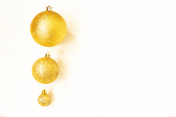 Three golden Christmas balls of different sizes are displayed in a row as a border on a white background. Copy space