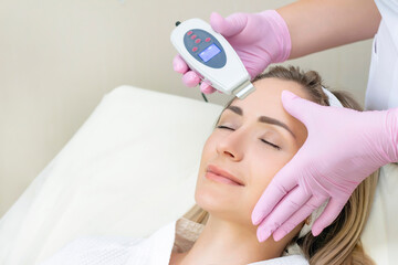 Cosmetologist makes an ultrasonic cleaning of the face of a young woman.