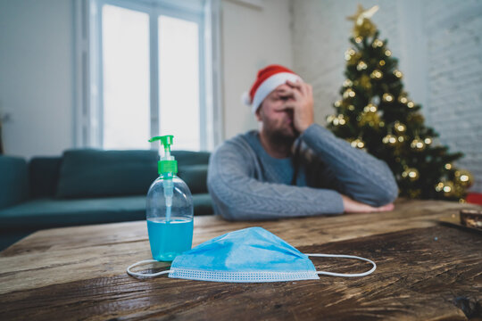 Conceptual image of Face mask and hand sanitizer in blur background of depressed man at christmas