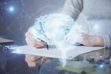 Double exposure of woman's writing hand on background with brain hud. Concept of learning.