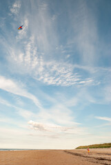 Little girl alone on a beach flying her kite in a beautiful blue sky
