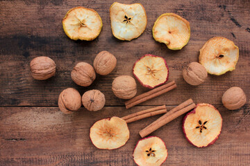 Dried fruits apples rings, walnuts,  and cinnamon sticks on wooden background. Top view. Rustic style. Selective focus