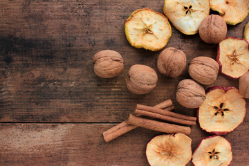 Fototapeta premium Dried fruits apples rings, walnuts, and cinnamon sticks on wooden background. Top view. Rustic style. Selective focus