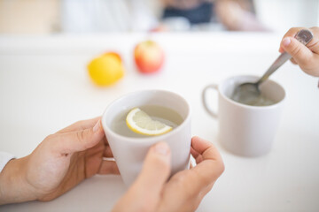Hands holding a cup of lemon tea on a white table