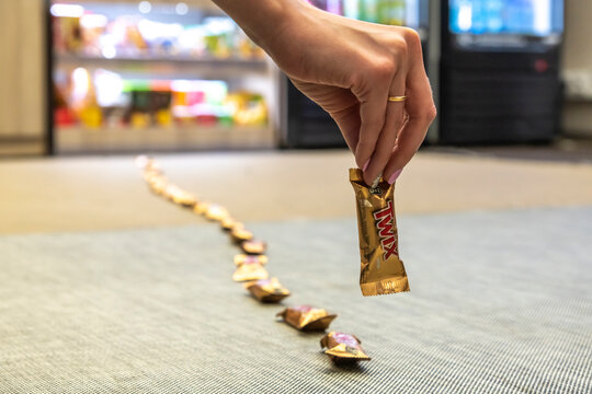 Moscow, Russia - November 19, 2020: Woman holds in her hand Twix Minis candy bar. Group of twix bars lies in line as bait leading to shelf of grocery store. Illustrative editorial photography.
