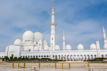 Panorama of White Grand Mosque with fence against blue sky, also called Sheikh Zayed Grand Mosque, inspired by Persian, Mughal and Moorish mosque architecture