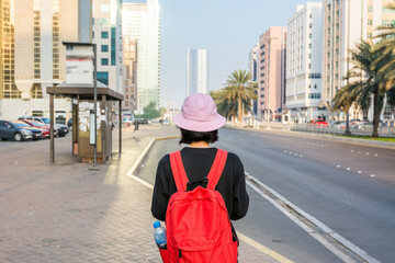 A Chinese girl wearing backpack and pink hat looking at the street view with skylines and bus...