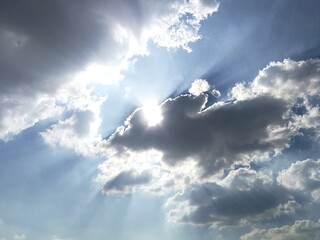 Scenic blue sky with clouds, dramatic sky with bright light from the sun behind the fluffy clouds.