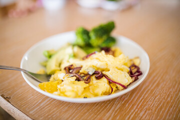 Broccoli and scrambled eggs with avocado slices on wooden table