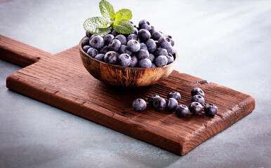Bowl of fresh blueberries on rustic wooden board. Organic food blueberries and mint leaf for healthy lifestyle.