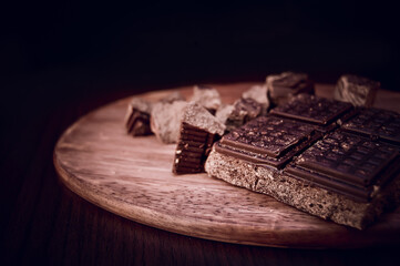 Black chocolate at wooden background. Moody dark food photo.