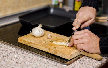 Fototapeta na wymiar Man cutting garlic with a knife on a wooden board