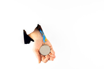 A hand holds a silver medal through a hole in a white wall. Free space for text