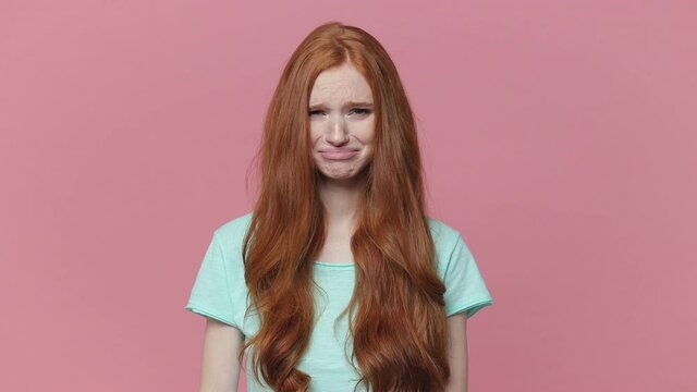 Displeased crying ginger redhead young woman wearing casual blue turquoise t-shirt posing isolated on pink color background studio. People lifestyle concept Keeping eyes closed spreading hands ask why