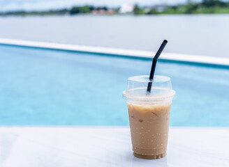 Iced coffee or Iced latte coffee in a plastic cup on the table at the cafe against clear blue water...