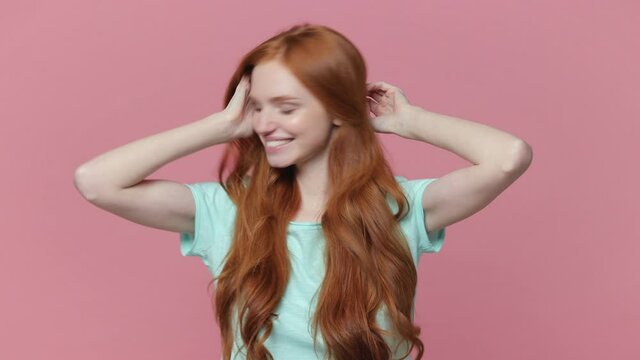 Smiling cheerful redhead young woman in casual blue turquoise t-shirt posing isolated on pastel pink background in studio. People lifestyle concept. Dancing clenching fists rising hands shaking head