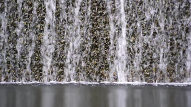 Water falling pouring into a poolside from stone wall, close up. Background with running water. Waterfall fountain stri and spray drops stone surface.