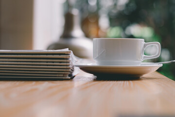 Coffee​ cup​ on the wood desk and newspaper with the bright light of the morning sun in the office or house,Cozy atmosphere is for relaxing on vacation or charge energy to refresh the body to working.