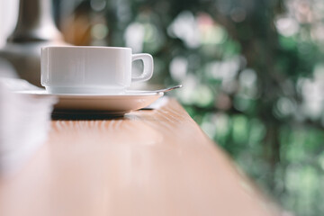 Coffee​ cup​ on the wood desk by the window with the bright light of the morning sun in the office or house,Cozy atmosphere is for relaxing on vacation,charge energy to refresh the body to working.