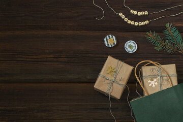 New Year's shopping. Gift green paper bag with kraft paper boxes with golden snowflakes on dark wooden background. Wooden beads with the inscription Happy Christmas. Copy space. Festive concept.