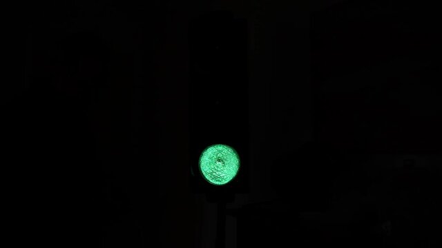 The red stoplight of a traffic light or a semaphore turns green at night in the city. Black background.