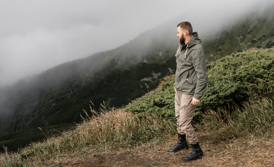 The traveler stands on a mountain peak and looks at the mountains in the fog.