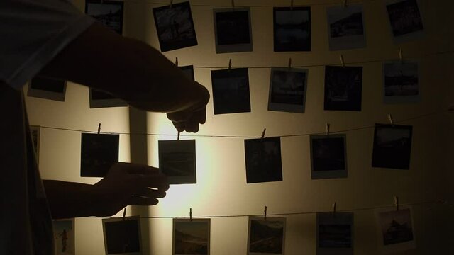 silhouette of asian man attach printed photo on rope string at glass wall decoration. home portfolio arts gallery displaying. all photos shot by Vajirawich Wongpuvarak.
