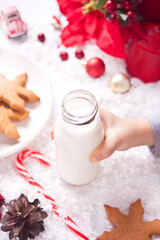Obraz na płótnie Canvas Cookies, candy cane and milk for Santa on table on the Christmas decoration background. Child hand take a bottle with milk.