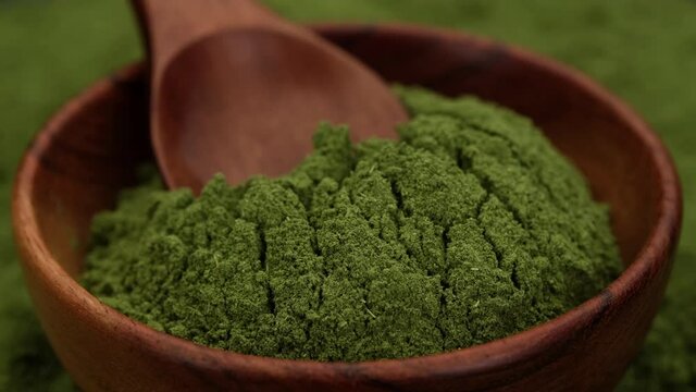 superfoods chlorella or spirulina powder in wooden bowl, rotating. green powder