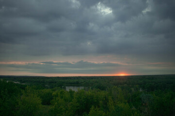 Naklejka na ściany i meble The sun almost went down the horizon, cloudy gray blue sky, forest and river in the distance
