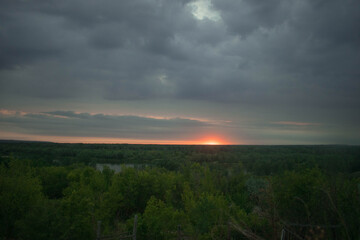The sun almost went down the horizon, cloudy gray blue sky, forest and river in the distance
