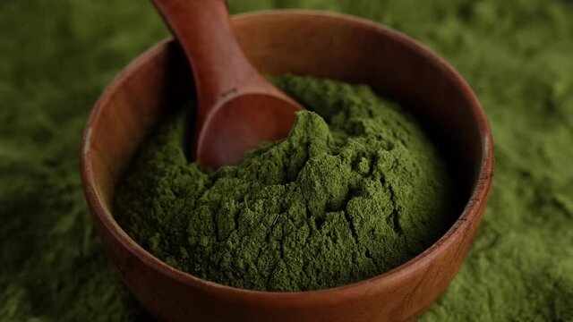 superfoods chlorella or spirulina powder in wooden bowl, rotating. green powder