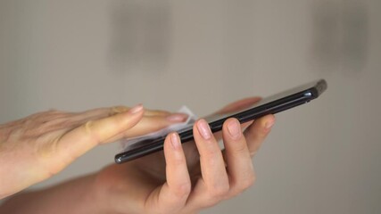 Close-up of woman hand using wet wipe and sanitizer to clean cell phone screen. People cleaning and disinfecting mobile telephone monitor to kill virus and germs. Female hands holding smartphone - Powered by Adobe