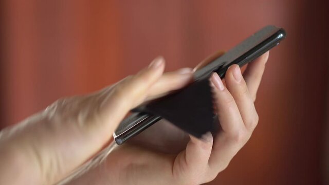 Close-up of woman hand using wet wipe and sanitizer to clean cell phone screen. People cleaning and disinfecting mobile telephone monitor to kill virus and germs. Female hands holding smartphone