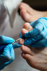 Hardware pedicure, preparation of the nail plate for applying gel polish. Master chiropody shapes the nails . Female patient in the process of hardware pedicure procedure. Foot care