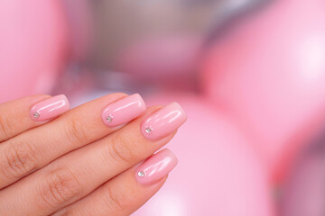 
Female hand with romantic manicure nails, nude gel polish, on pink balloons background