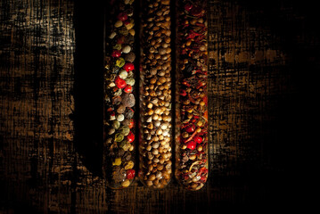 A mixture of various spices in a glass jar close up. Spices on a black, old shabby board. Free space and copy space for text near condiments. Contrasting dramatic light as an artistic effect.