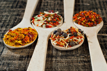A mixture of various spices in a wooden spoon. Spices and seasonings on an old shabby board. Mix on a pile close up.