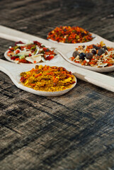 A mixture of various spices in a wooden spoon. Spices and seasonings on an old shabby board. Mix on a pile close up. Place for text and copy space near the spoon.