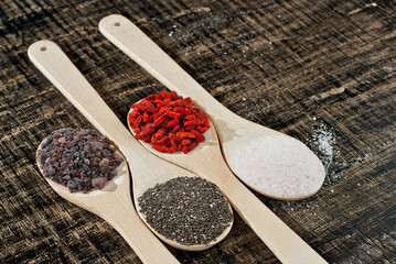 Goji berries, chia seeds, Tibetan black salt, pink Himalayan salt on wooden spoons. Spices on an old shabby board. Place for text and copy space near the spoon.