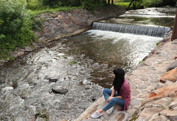  on the waterfall. girl sits on the edge of a mountain river with rapids. piece waterfalls, river bank. brunette in shirt and casual style. fast flow