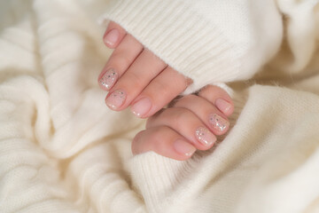 Closeup top view of beautiful faded pastel color trendy manicure of pink nails with glossy silver shiny design isolated on knitted white texture. Winter, autumn, spring style of naildesign concept.