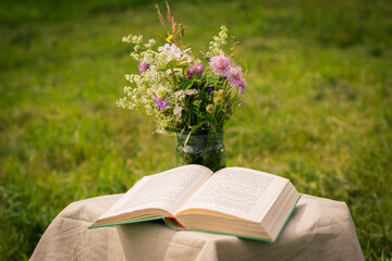 Naklejka na ściany i meble A beautiful bouquet of wildflowers and the open book on a soft summer background of summer garden.
